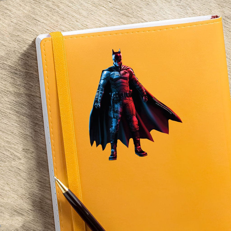 shaped vinyl sticker featuring a colorful Batman Standing shown on a bright yellow notebook with pen on a wood surface.