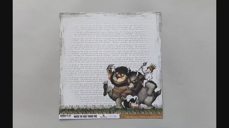 Female hands picking up scrapbook paper featuring Where the Wild Things Are on one side and a word pattern on the other side.