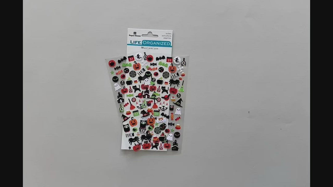 Female hands pick up and show in detail front and back of mini stickers featuring halloween cats, spiders, and pumpkins.