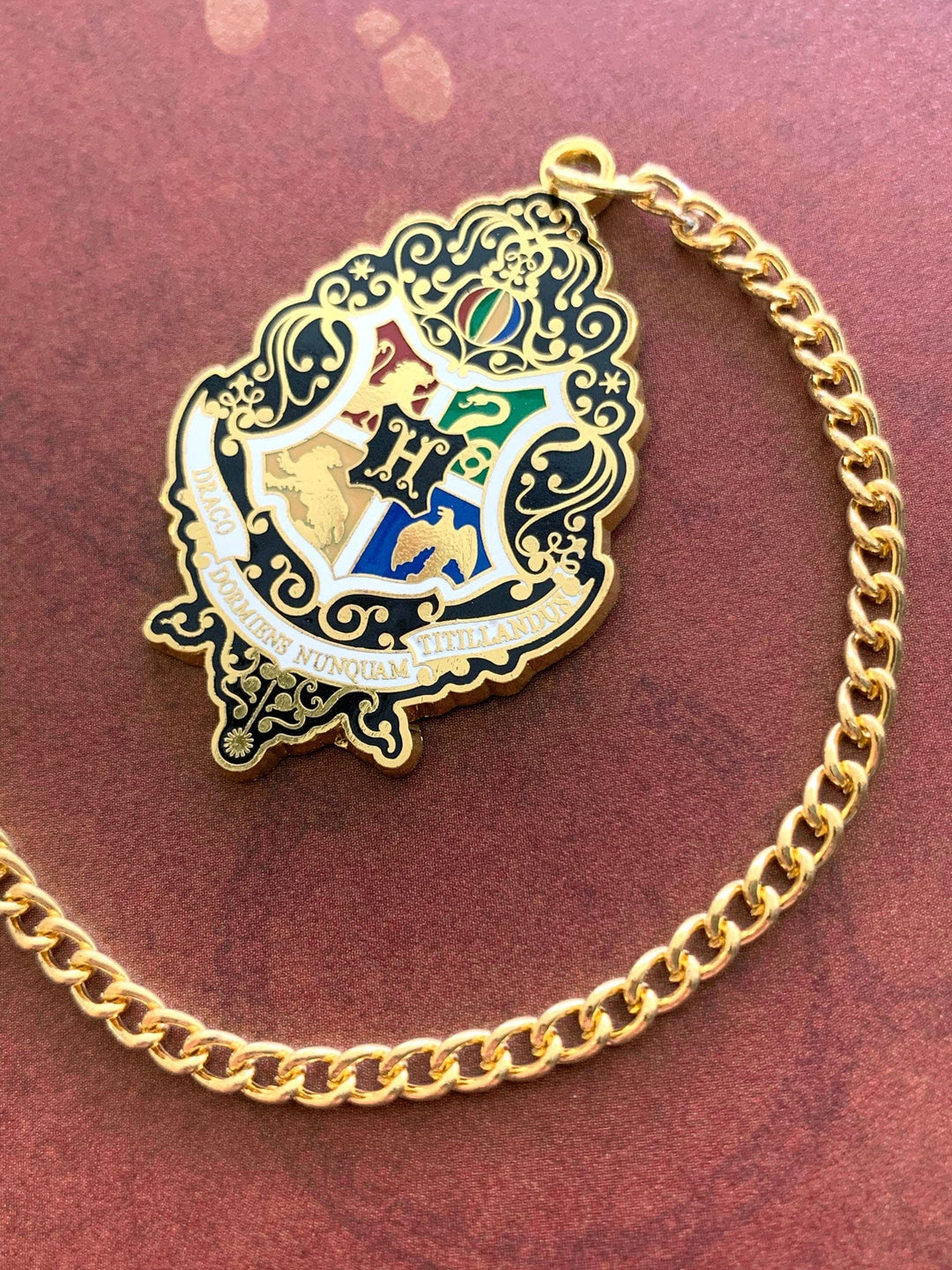 Harry Potter bookmark featuring colorful crest with gold details and gold chain, shown on rust colored background.
