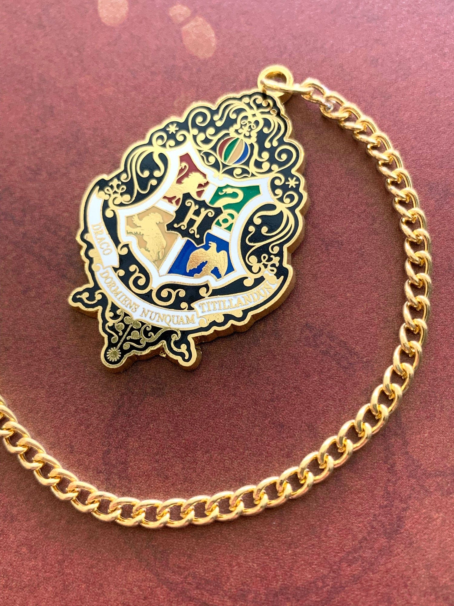 Harry Potter bookmark featuring colorful crest with gold details and gold chain, shown on rust colored background.