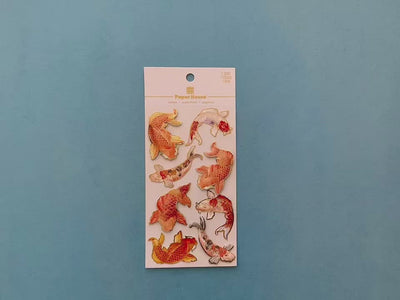 female hands display scrapbook stickers featuring orange and gold koi fish, and shows close up of one individual sticker.