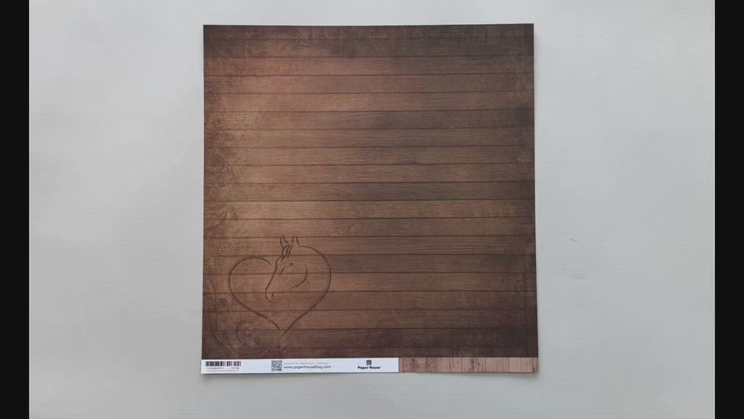 Female hands pick up scrapbook paper featuring a brown wood pattern with a heart etched on it on one side and cowboy boots and a hat with a wood pattern on the other side.