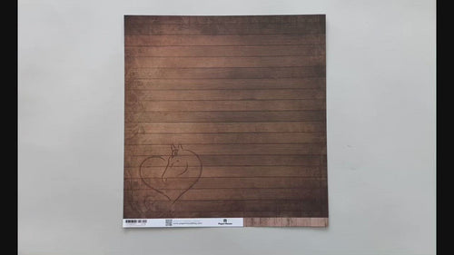 Female hands pick up scrapbook paper featuring a brown wood pattern with a heart etched on it on one side and cowboy boots and a hat with a wood pattern on the other side.