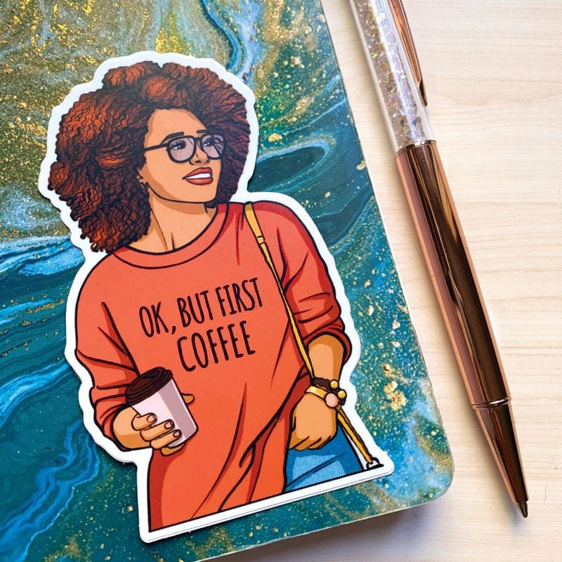 Shaped laptop sticker featuring woman holding a coffee cup and wearing an orange sweatshirt with coffee sentiment, shown on a blue and gold marbled notebook with rose gold pen beside it.