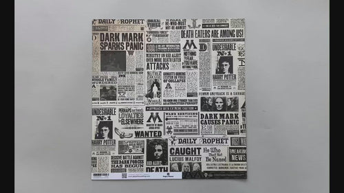 Female hands pick up harry potter scrapbook paper featuring black and white newsprint on the front and a pattern of the Deathly Hallows symbol on the back.
