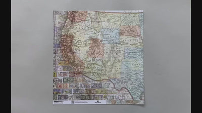 Female hands pick up scrapbook paper featuring a detailed map of the west coast of the USA on one side and the east coast on the other side.