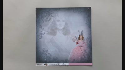 Female hands pick up scrapook paper featuring Glinda of The Wizard of Oz on one side and a solid pink on the other side.