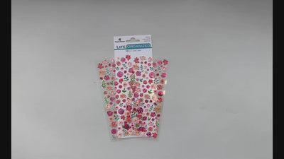 Female hands pick up and show in detail the front and back of sheet of mini stickers featuring pink flowers.