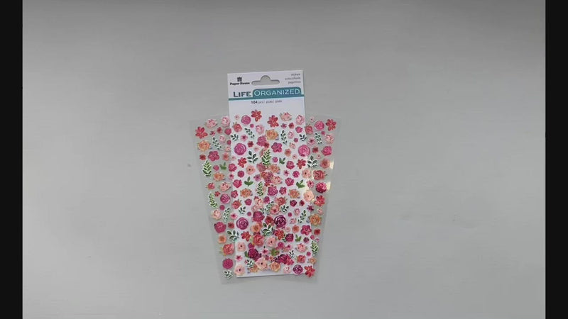 Female hands pick up and show in detail the front and back of sheet of mini stickers featuring pink flowers.