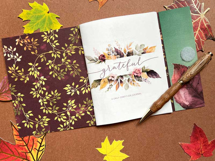 DHT-0002E - Gratitude Journal - Printable - Autumn-themed gratitude journal with watercolor florals, surrounded by fall leaves and a wooden pen on brown background
