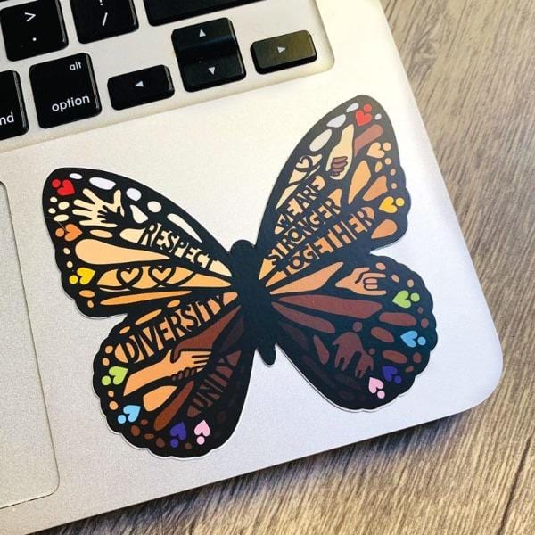 Shaped butterfly laptop sticker featuring holding hands, hearts, and words of wisdom such as respect and diversity, shown on a silver laptop computer.