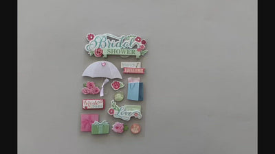 Female hands pick up and show front and back of 3D scrapbook stickers featuring bridal shower umbrella, gifts and flowers.