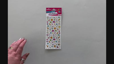 Female hands showing front and back of mini stickers featuring colorful illustrated planets, stars and rocketships and placing on surface with package.