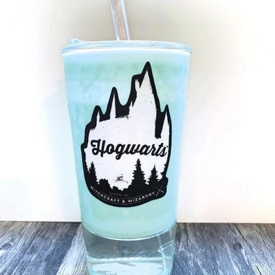Shaped Harry Potter laptop sticker featuring a silhouette of the Hogwarts castle in black and white is shown on a drinking glass filled with blue liquid and a straw.