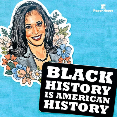 "BLACK HISTORY IS AMERICAN HISTORY" laptop sticker in white letters on a black background, is shown overlapping another laptop sticker featuring Kamala Harris. Both are shown on a blue background.