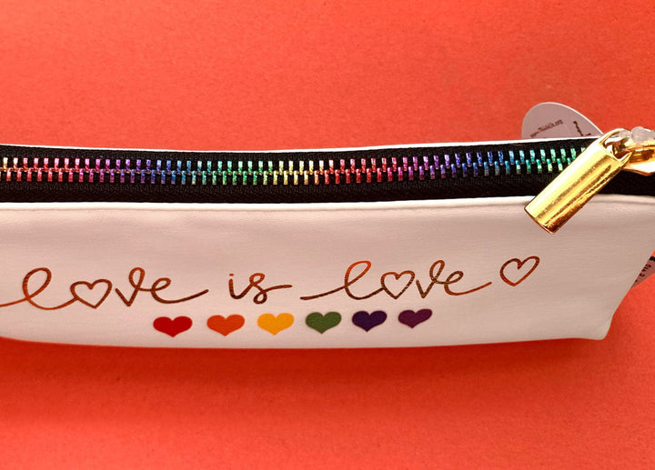 White pencil pouch featuring a metallic, rainbow zipper shown on a red background.