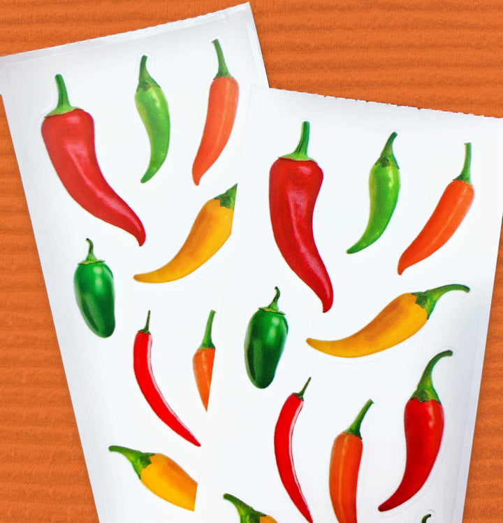 close up of 2 sheets of stickers featuring colorful hot peppers, shown on orange background.