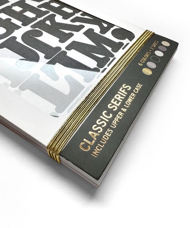 STBK-1000E - Alphabet Stickers - Alphabooks Classic Serifs - Closed book with black cover featuring gold text and striped spine, displaying black serif alphabet letter stickers on white pages