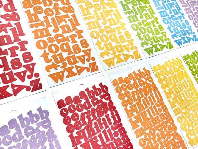 STBK-1001E - Alphabet Stickers - Alphabooks Colorways Serifs - Colorful alphabet letter stickers in rainbow hues including red, orange, yellow, green, blue, and purple displayed in overlapping sheets