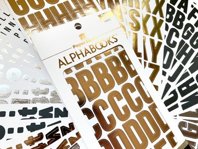 STBK-1002E - Alphabet Stickers - Alphabooks Classic Block - Gold and black alphabet letter stickers displayed on packaging cards showing various typeface styles and sizes