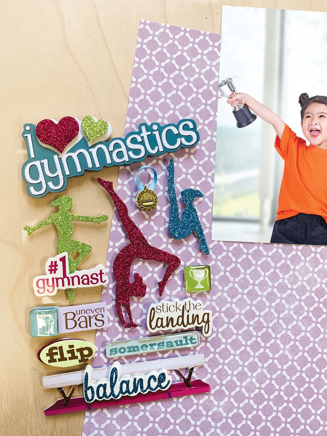 3D scrapbook stickers featuring colorful, glitter silhouettes of gymnasts shown next to a photo of a child holding a trophy.