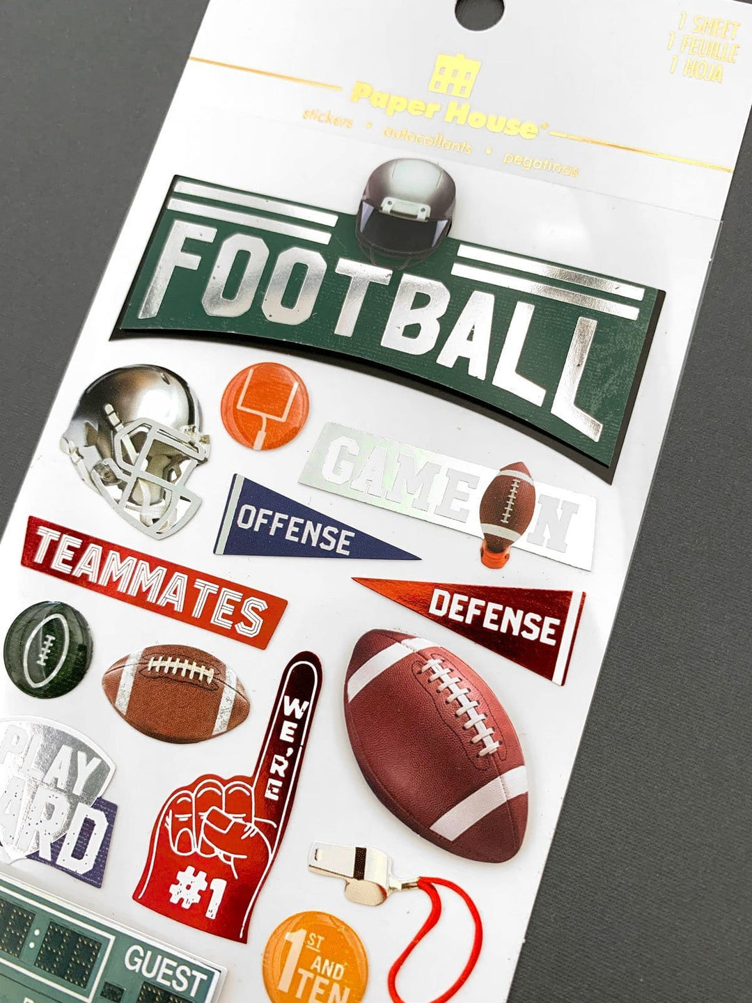 Scrapbook sticker featuring words, helmets, footballs and silver &amp; red foil with green, red and blue details. Shown in white package on gray background.