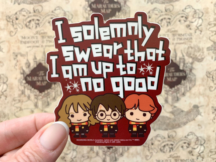 close up of Shaped Harry Potter laptop sticker shown in hand, featuring 3 chibi characters and "I solemnly swear…" sentiment, shown above a beige marauder&