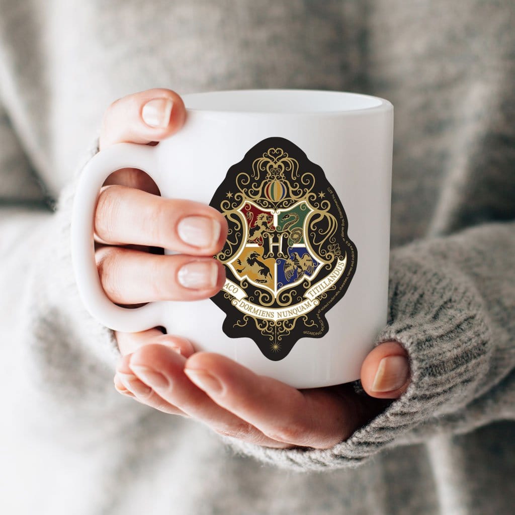 vinyl laptop sticker featuring Harry Potter Knockturn Hogwarts Crest shown adhered to a white mug held in a hand.