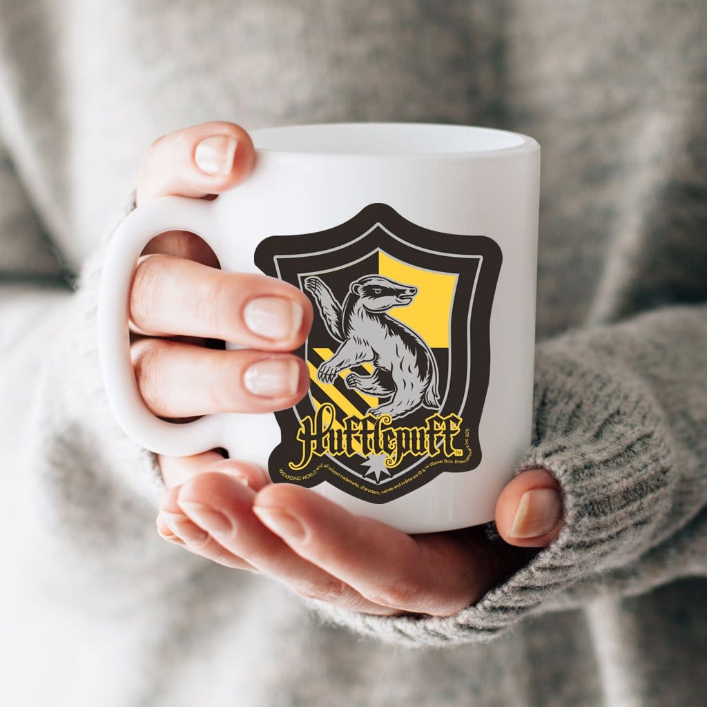 vinyl laptop sticker featuring Harry Potter Hufflepuff Shield shown adhered to a white mug held in a hand.