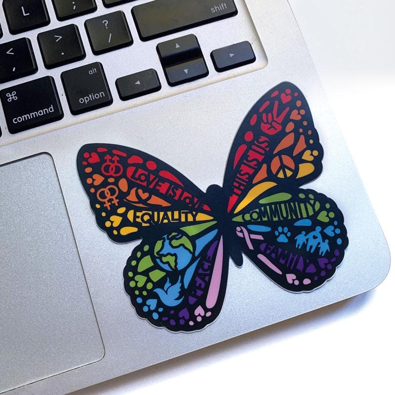 Shaped butterfly laptop sticker featuring rainbow colors and words of equality and peace, shown on a silver laptop computer.