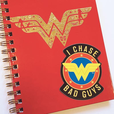 Shaped laptop sticker featuring the Wonder Woman logo and "I CHASE BAD GUYS" text is shown on a red notebook with a large, gold Wonder Woman logo.